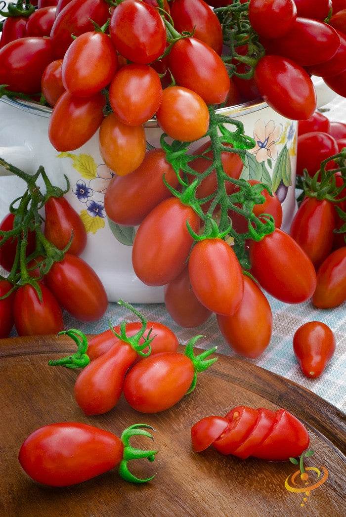 Red Pear Tomato Seeds | Cluster of ripe red pear tomatoes with one sliced on a wooden board and a decorative cup in the background