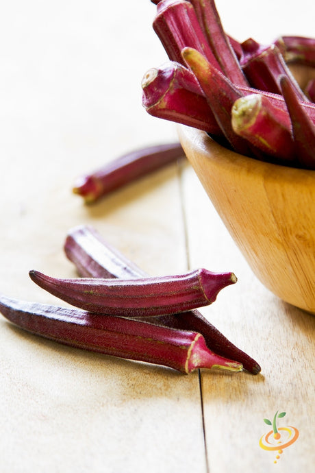 Fresh red burgundy okra pods in a wooden bowl on a light wooden surface